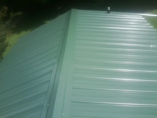 New green metal panels meeting at the ridge of a roof — Flat Roof Repair work by our crew in Renton