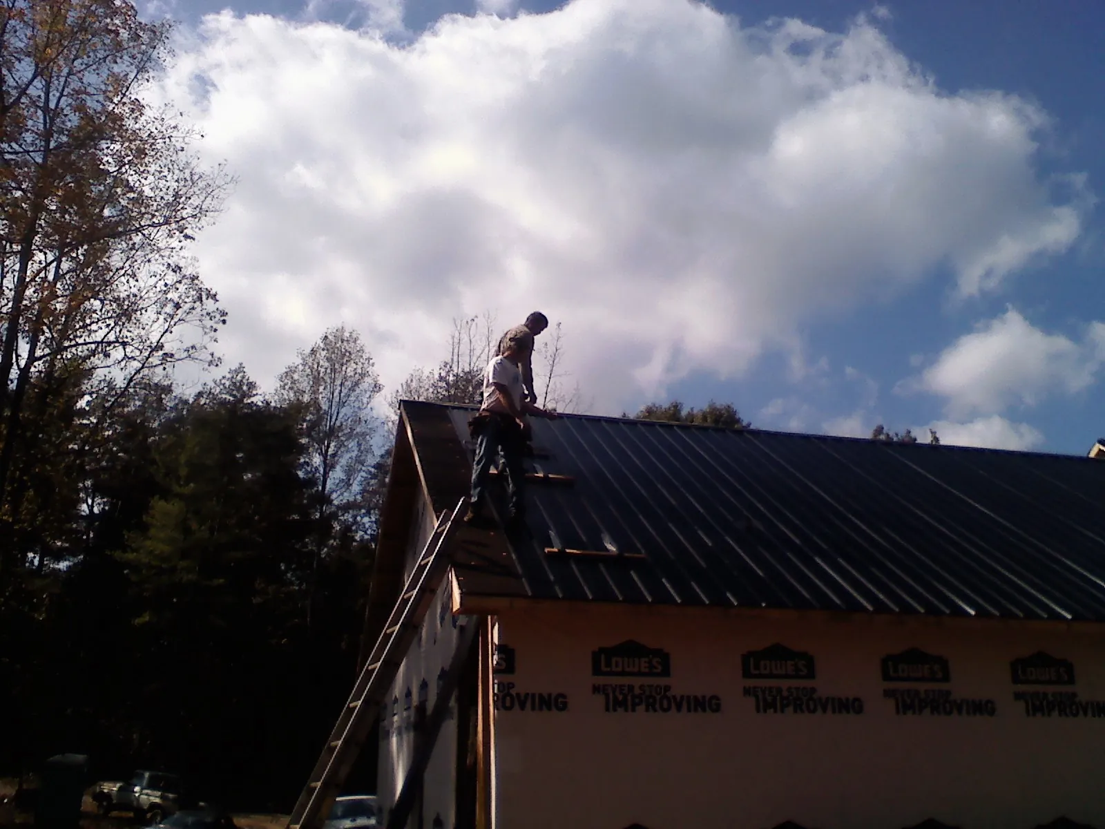 Roofer fastening dark metal panels high against a cloudy sky, from a Roof Inspection job in Renton