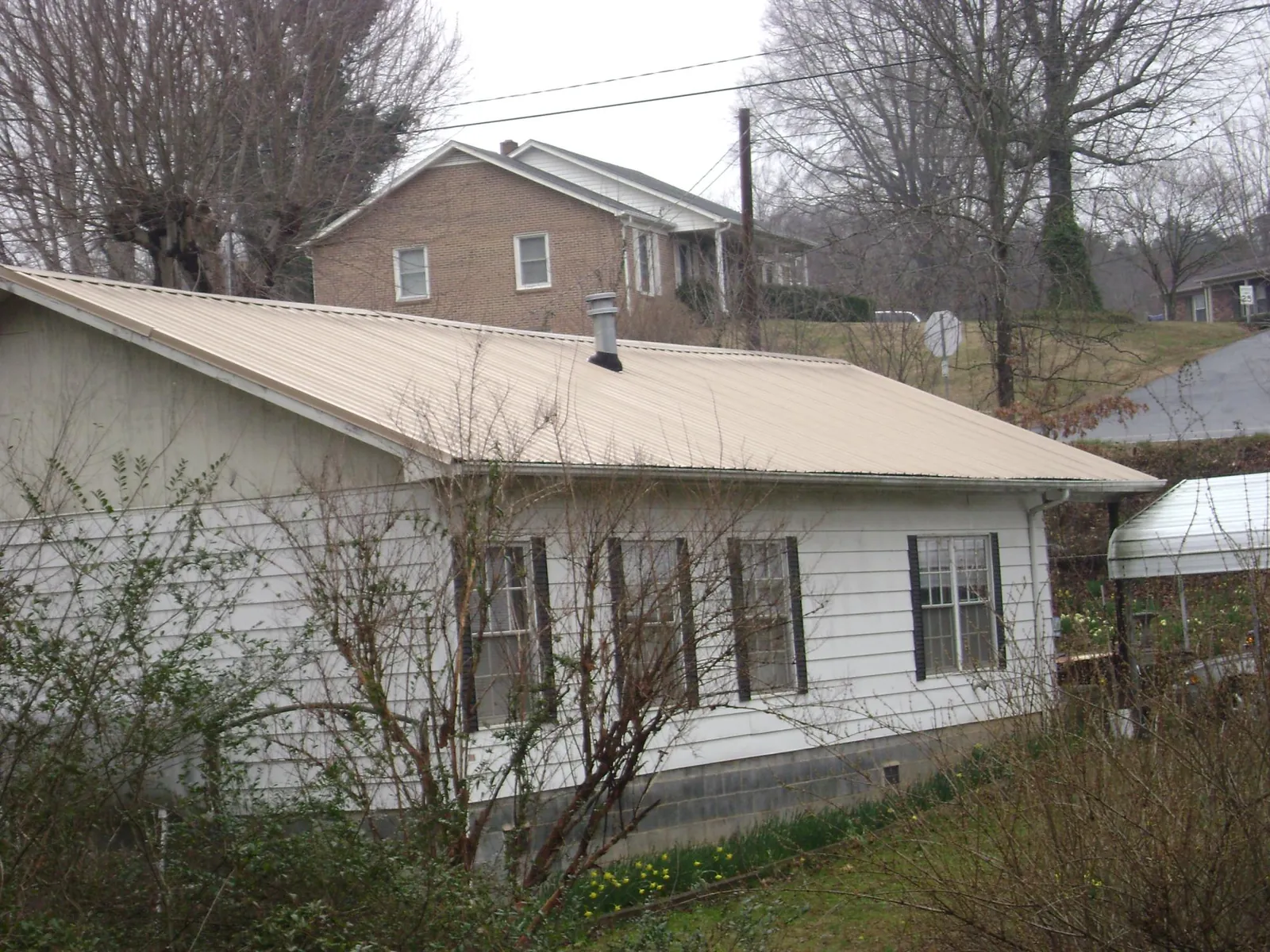 Tan metal roof on a white sided house set into a hillside — Commercial Roofing by Roofing Brothers in Renton